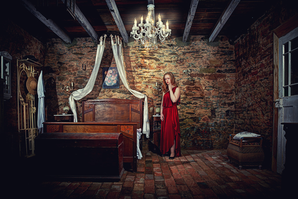 rothaariges Model mit rotem Kleid in romantischem Schlafzimmer