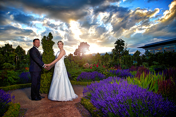 Braut und Bräutigam stehen vor tollem Himmel im Garten